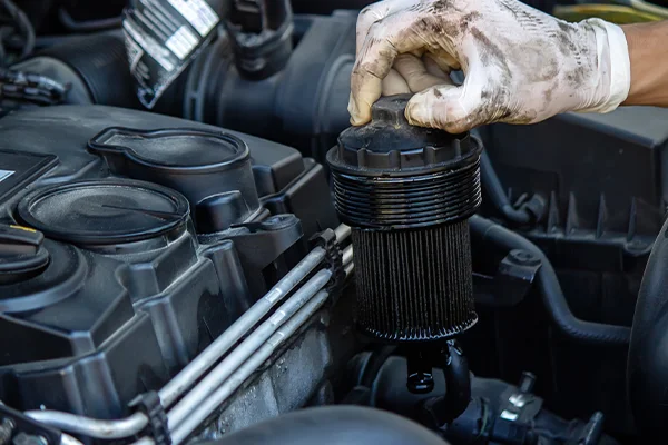 Hand removing dirty oil filter from vehicle's engine bay