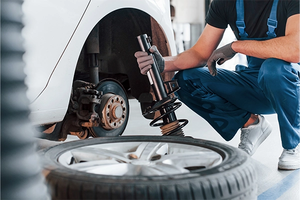 A technician holding a suspension spring next to a vehicle 